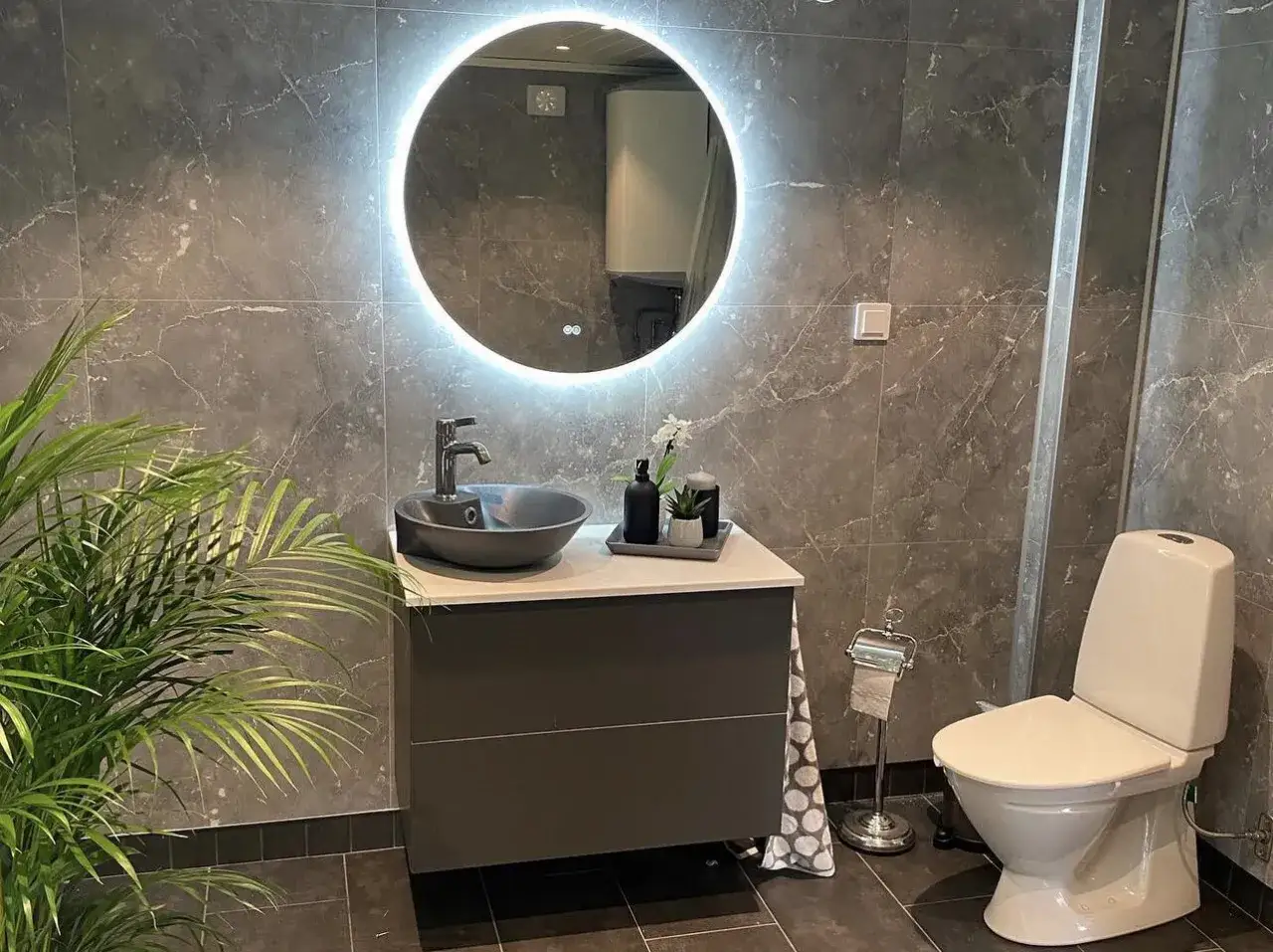 Modernt badrum med grå marmor, belyst spegel, handfat och toalett. Perfekt för att få inspiration för renovera badrum pris.