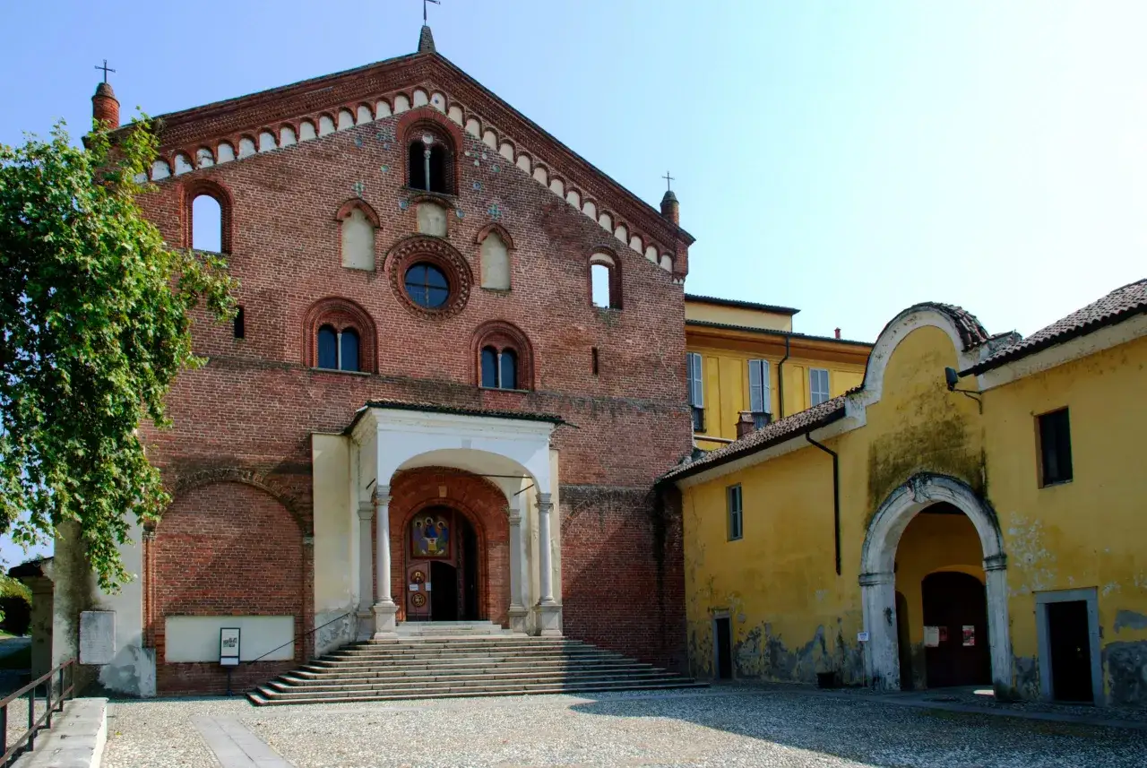 Morimondo cosa vedere: imponente chiesa in mattoni rossi con scalinata e portico, adiacente edificio giallo.