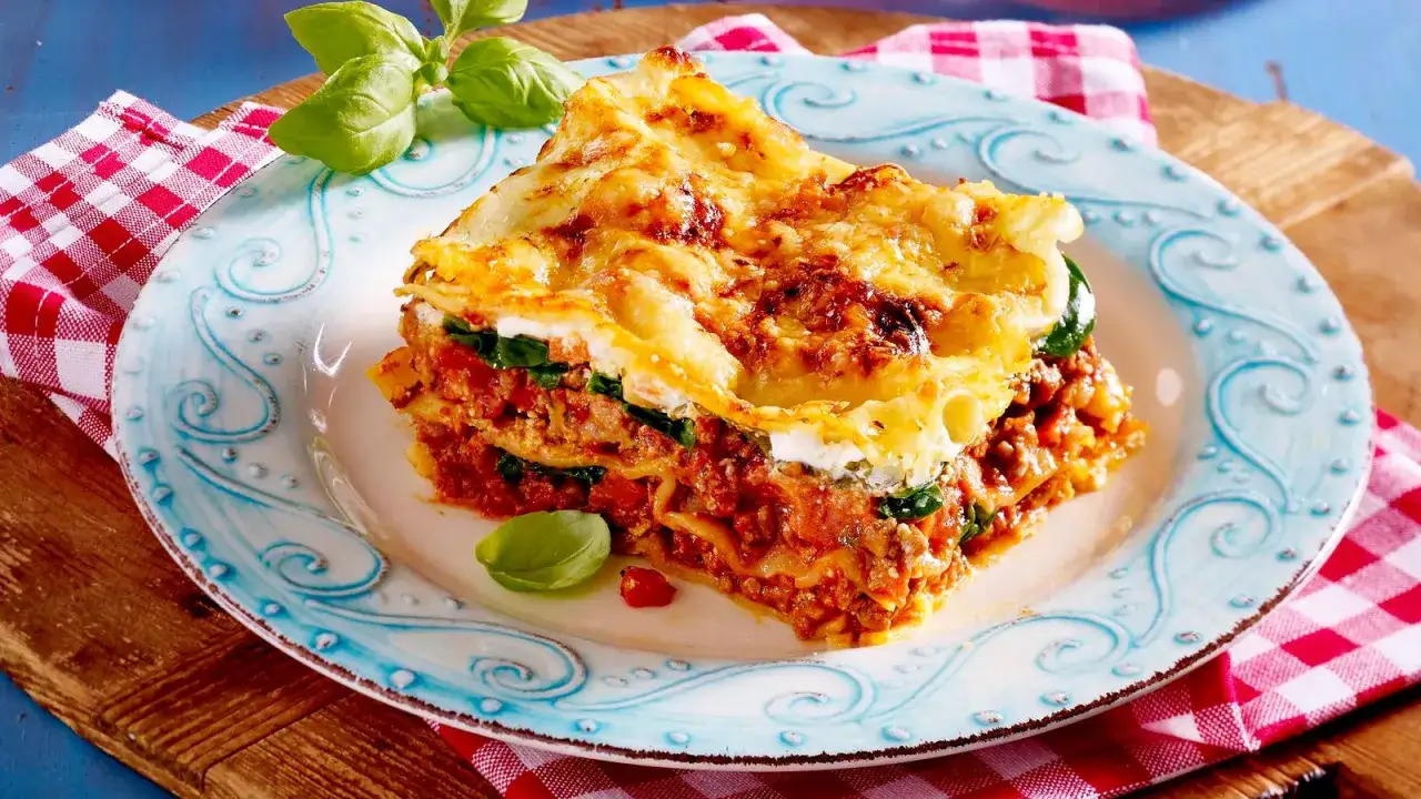 Ein Stück Lasagne mit Hackfleischsauce und Spinat, überbacken mit Käse und einem Klecks Creme Fraiche. Garniert mit Basilikum.