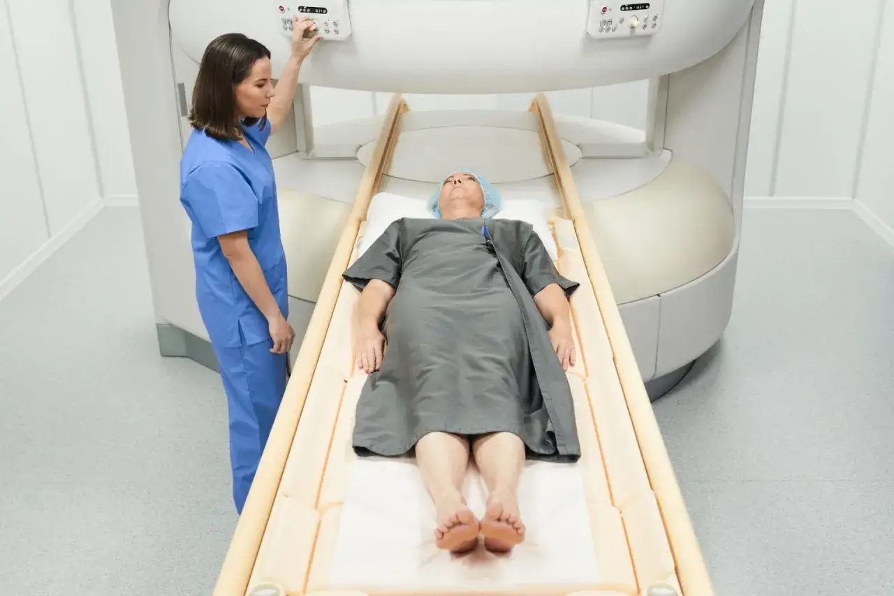 Pacjent leży na stole do rezonansu magnetycznego, pielęgniarka przygotowuje badanie. Rezonans biodra pomoże zdiagnozować problem.