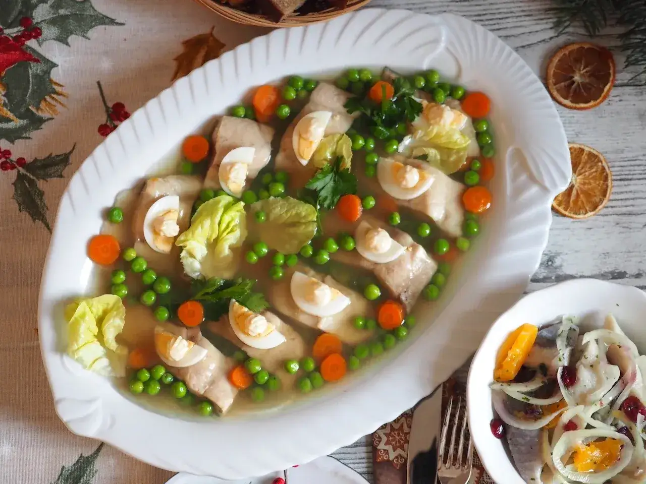Elegancka ryba w galarecie z groszkiem, marchewką i jajkiem. Obok miseczka śledzia z cebulą i pomarańczą.