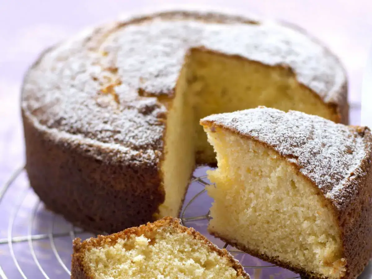 Un délicieux gâteau sans oeuf, saupoudré de sucre glace, attend sur une grille. Une part est déjà coupée, révélant sa mie moelleuse.