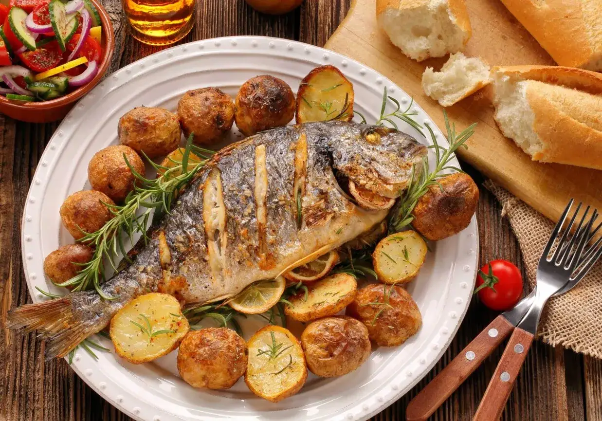 Idealna ryba na grilla: dorada pieczona z ziemniakami i rozmarynem, podana z sałatką i pieczywem.