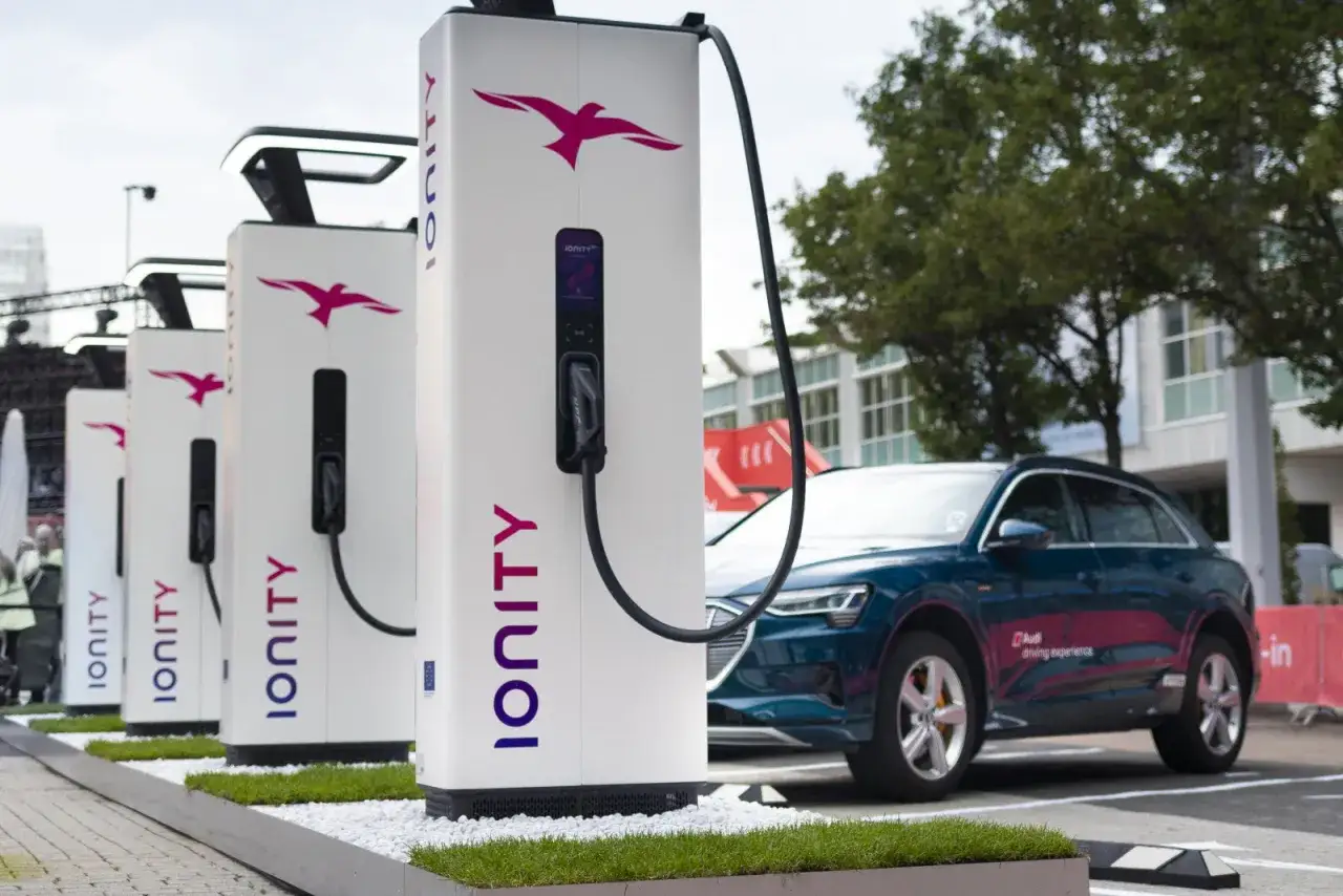 Une file de bornes de recharge Ionity pour une place voiture électrique. Une Audi bleue est garée à côté, prête à être chargée.