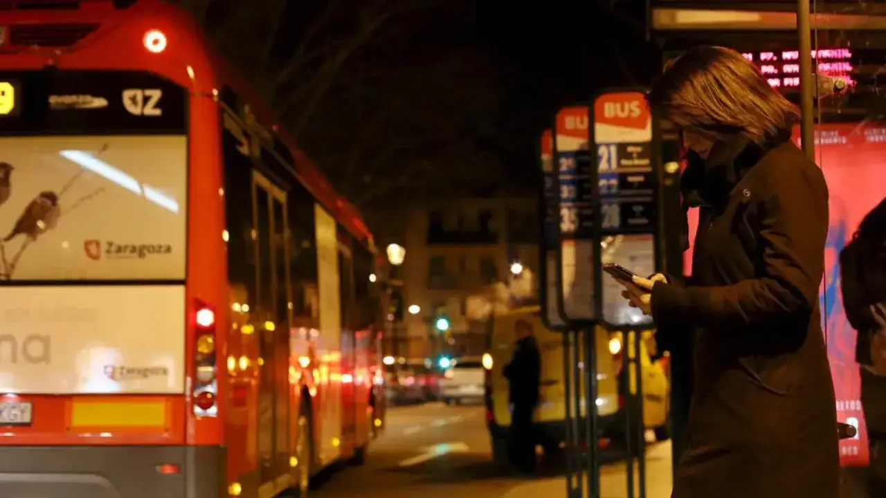 Mujer esperando los autobuses nocturnos Zaragoza, revisando su móvil en la parada.