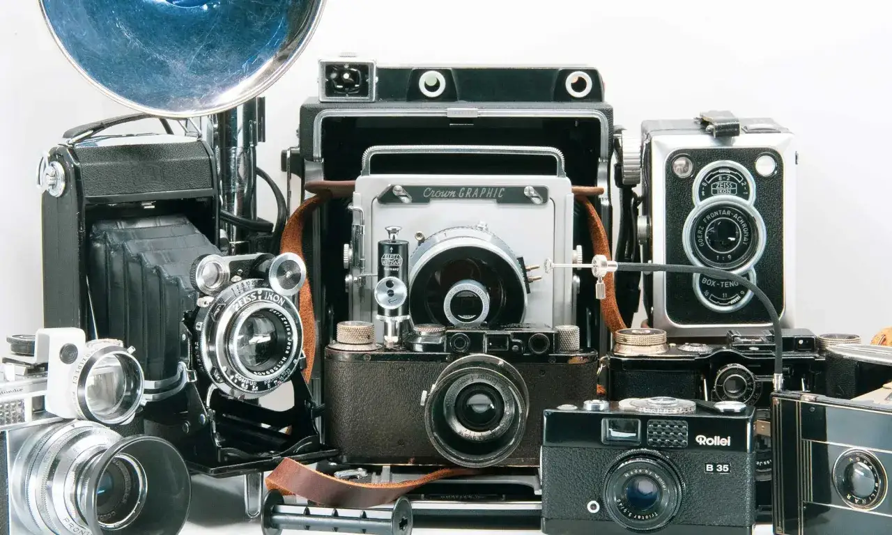 A collection of vintage cameras, including a Crown Graphic and a Pentacon Six, are displayed.