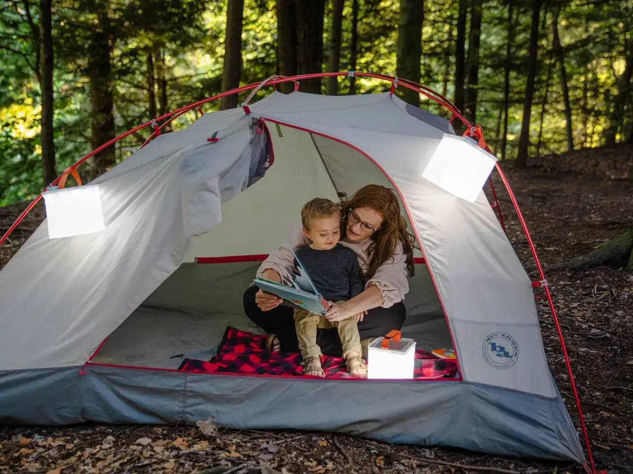 Mamma och barn l&auml;ser bok i t&auml;ltet. En mysig stund som en del av packlista camping.
