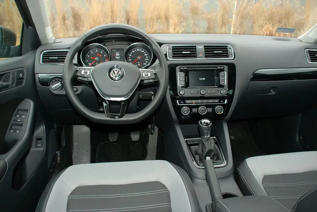 Wnętrze VW Jetta MK6: kierownica, deska rozdzielcza z ekranem dotykowym, dźwignia zmiany biegów i fotele.