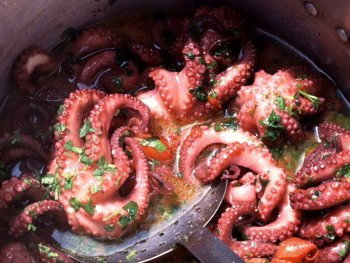 Gros plan sur une daube de poulpe mijotant dans une marmite, garnie de persil frais. Les tentacules roses sont tendres et app&eacute;tissants.