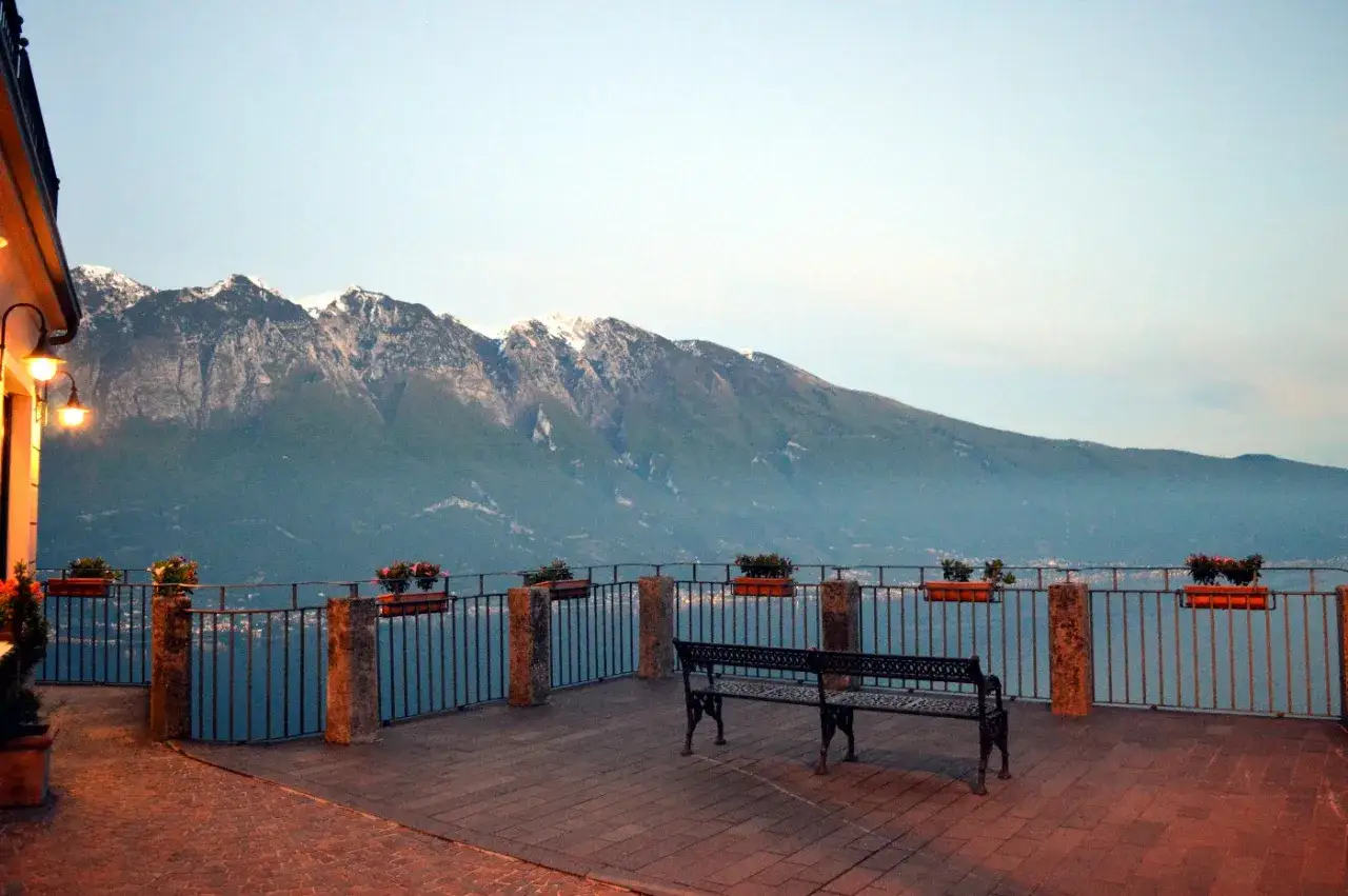 Panoramica serale con panchine e fiori su un terrazzo affacciato sul lago, con montagne innevate sullo sfondo. Ideale per passeggiate sul lago di Garda sponda bresciana.