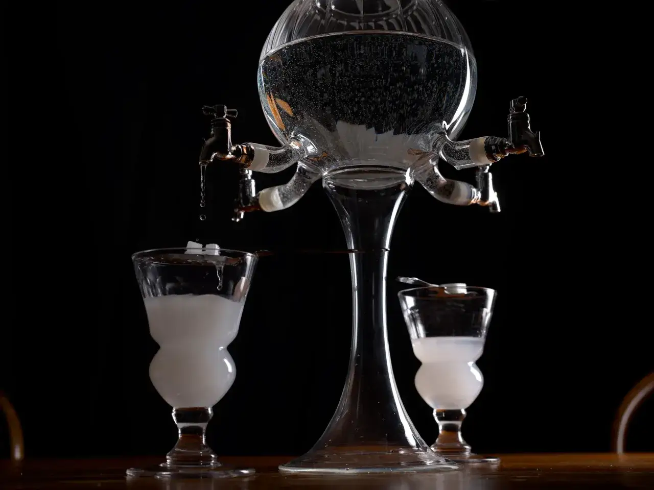 Ein Absinth-Brunnen mit zwei Gl&auml;sern, bereit f&uuml;r die Zubereitung. Die Geschichte des Absinth-Ursprungs wird hier lebendig.