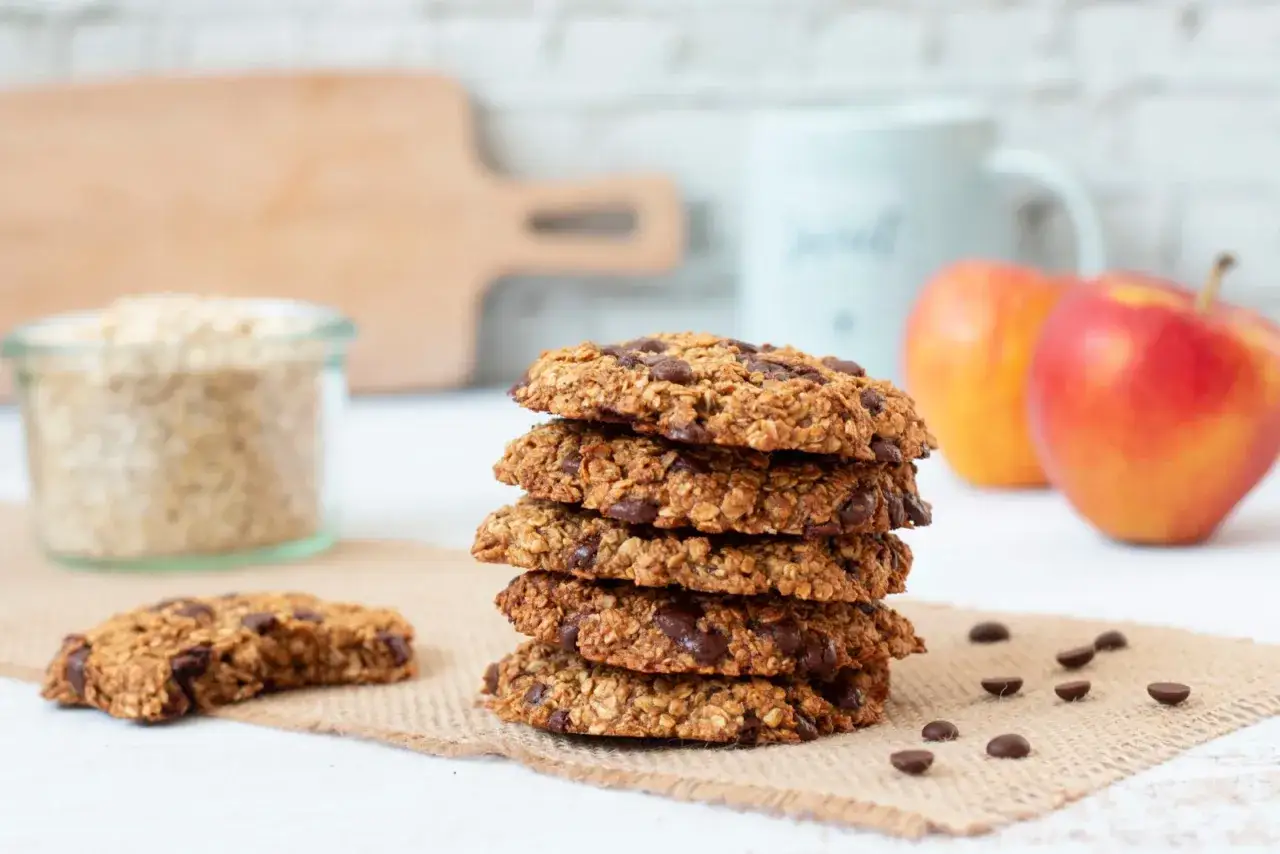 Pile de cookies sains aux flocons d'avoine et pépites de chocolat, accompagnés de compote de pommes et de fruits frais.