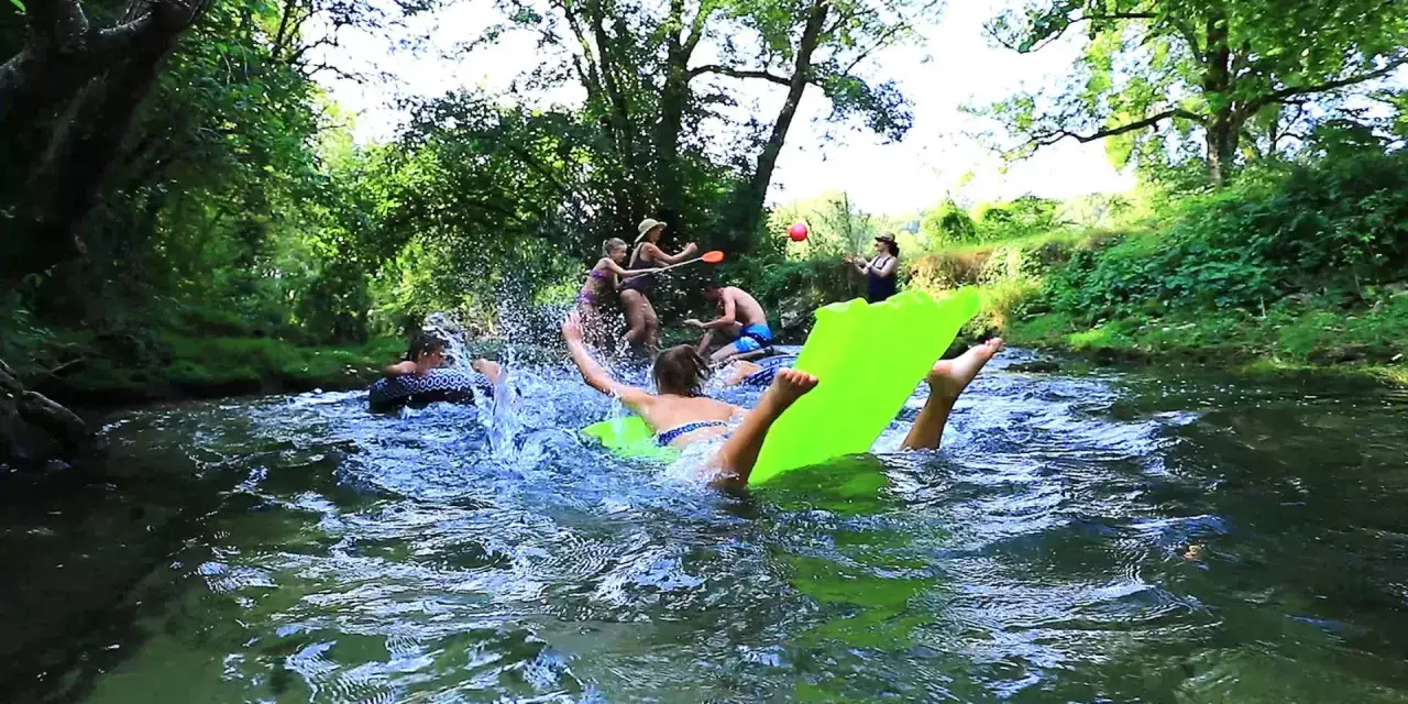 Amusante visite insolite autour de Sarlat : des jeunes s'éclaboussent et flottent sur des matelas dans une rivière verdoyante.