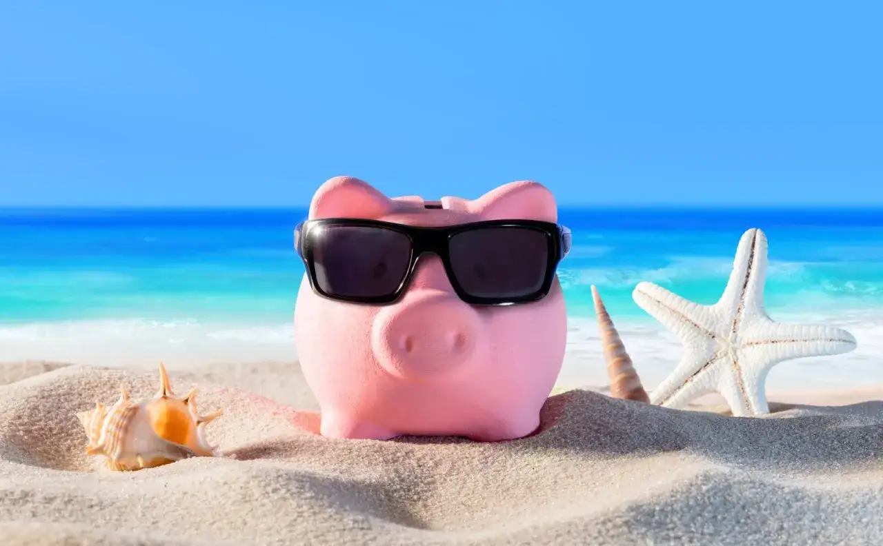 Różowa świnka-skarbonka w okularach przeciwsłonecznych na plaży, obok muszli i rozgwiazdy. Idealna na wczasy pod gruszą zasady.