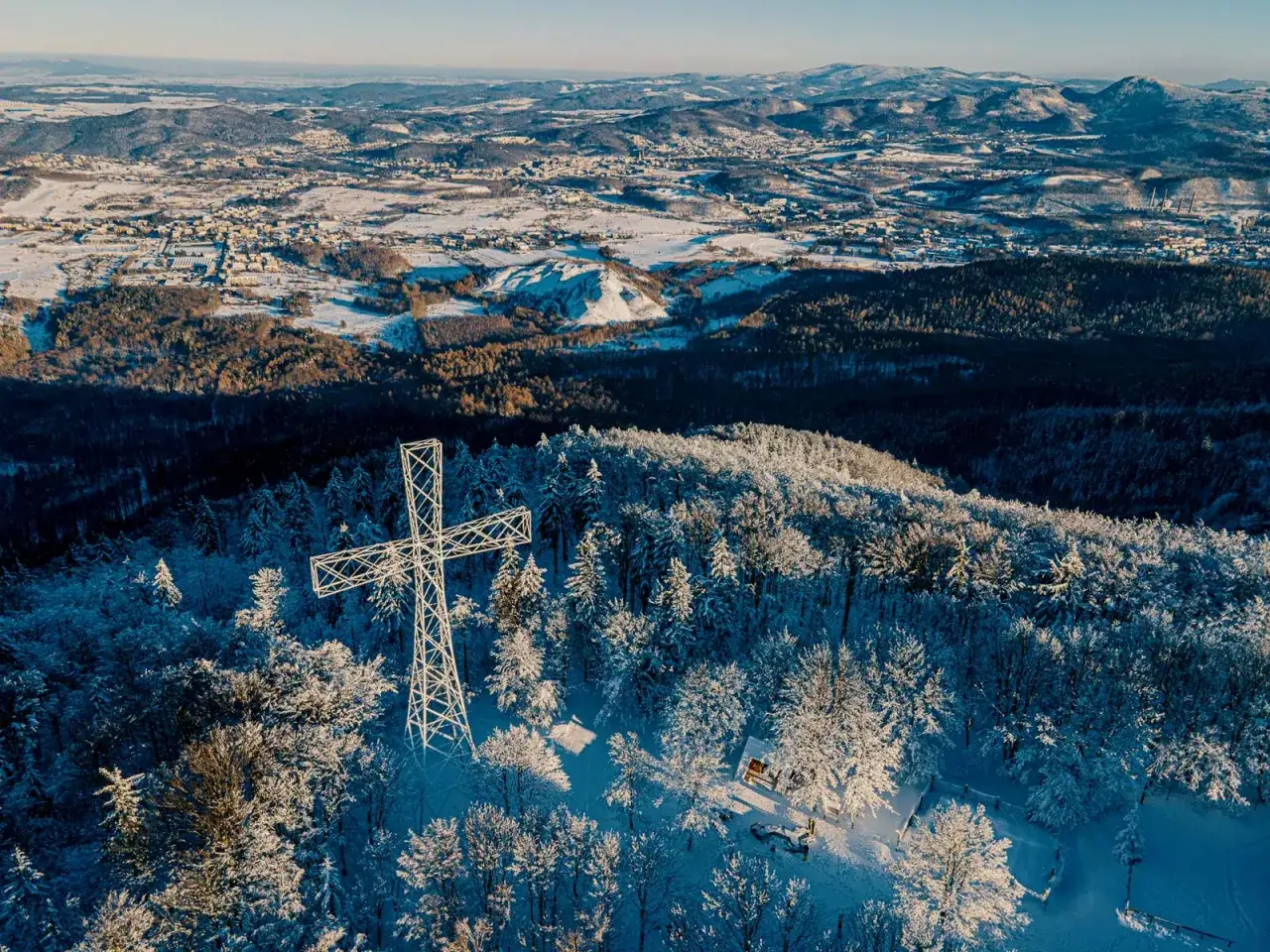 Zimowa trasa na Chełmiec. Ogromny metalowy krzyż góruje nad ośnieżonym lasem i panoramą gór.