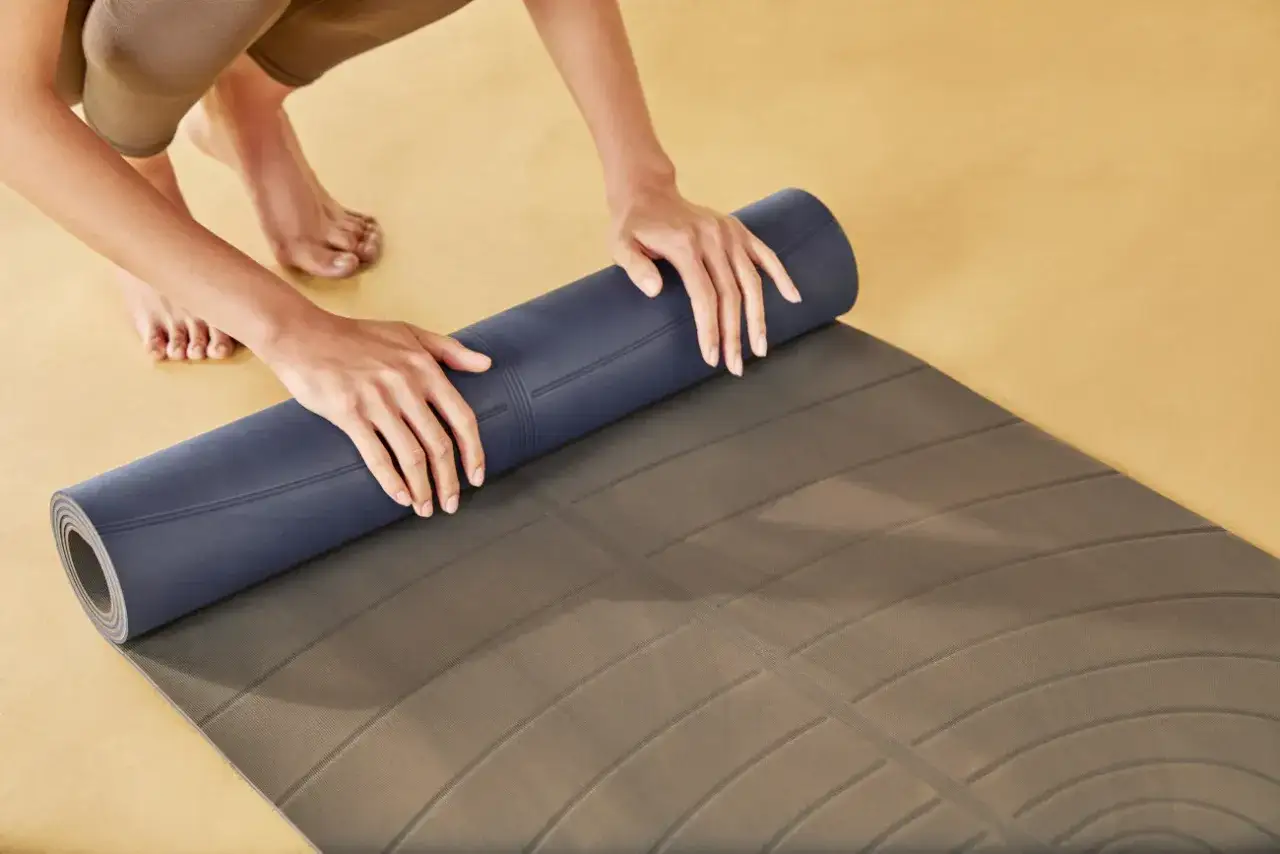 Hände rollen eine dunkelblaue Naturkautschuk Yogamatte auf, um sie zu reinigen.