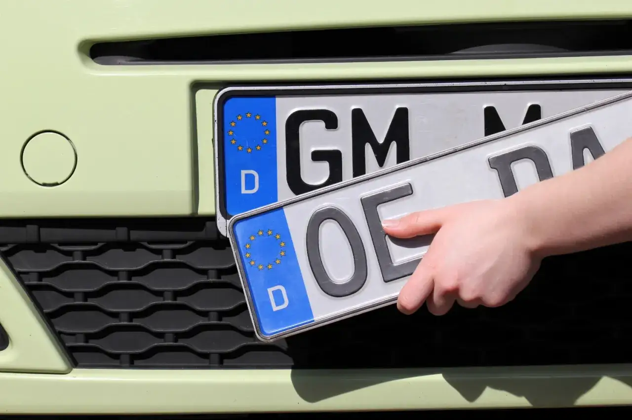 Hand wechselt Kennzeichen für das Auto ummelden. Ein neues Kennzeichen wird angebracht.