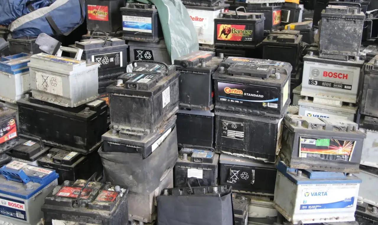 Stos starych akumulatorów samochodowych, gotowych do recyklingu. Widać napisy marek jak Bosch, Varta, Centra. To miejsce, gdzie można oddać zużyty akumulator, a czasem nawet otrzymać zwrot kaucji za akumulator.