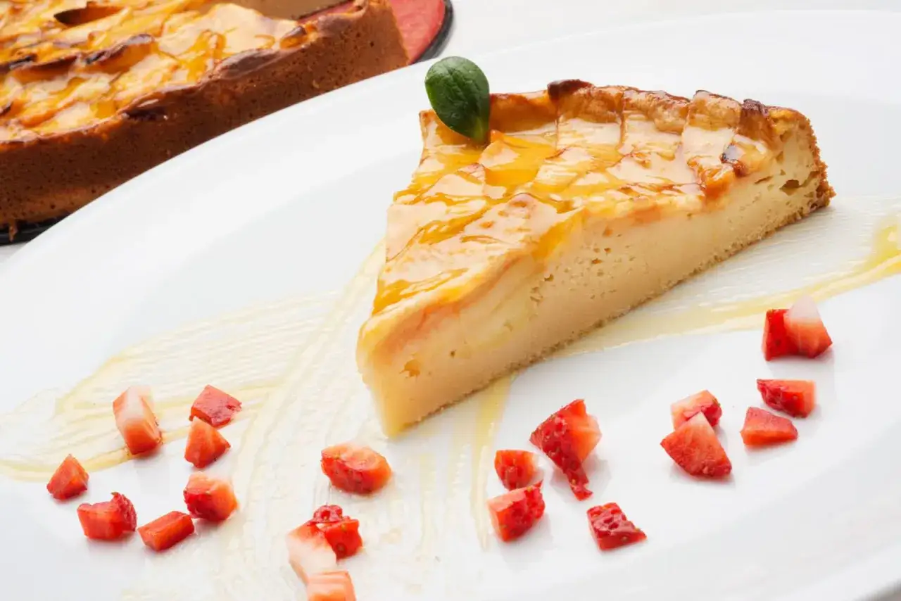 Rebanada de tarta de manzana dorada y brillante, decorada con fresas picadas y un toque verde.