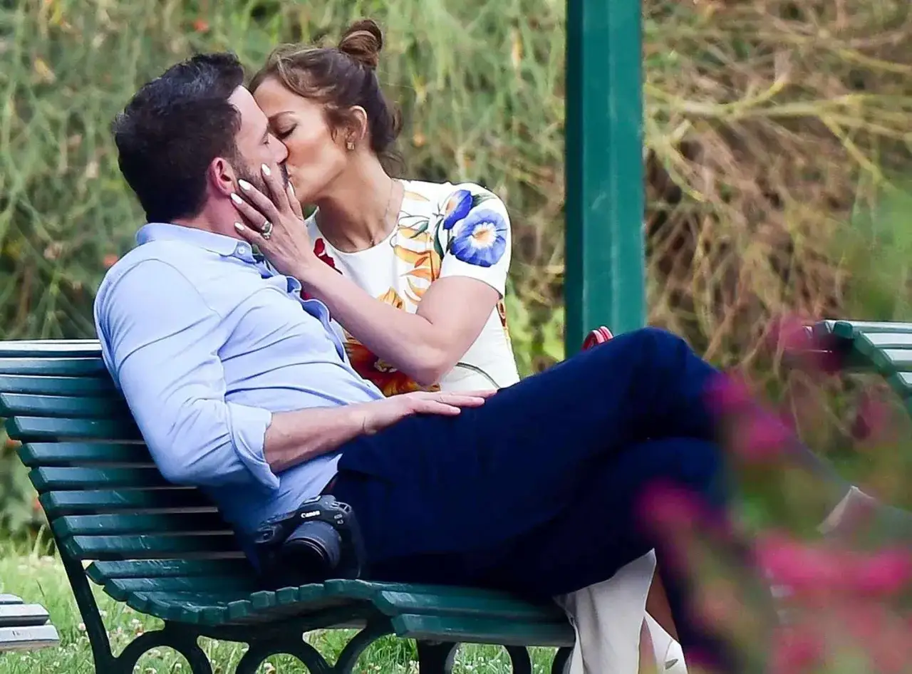 Jennifer Lopez i Ben Affleck całują się na ławce w parku.