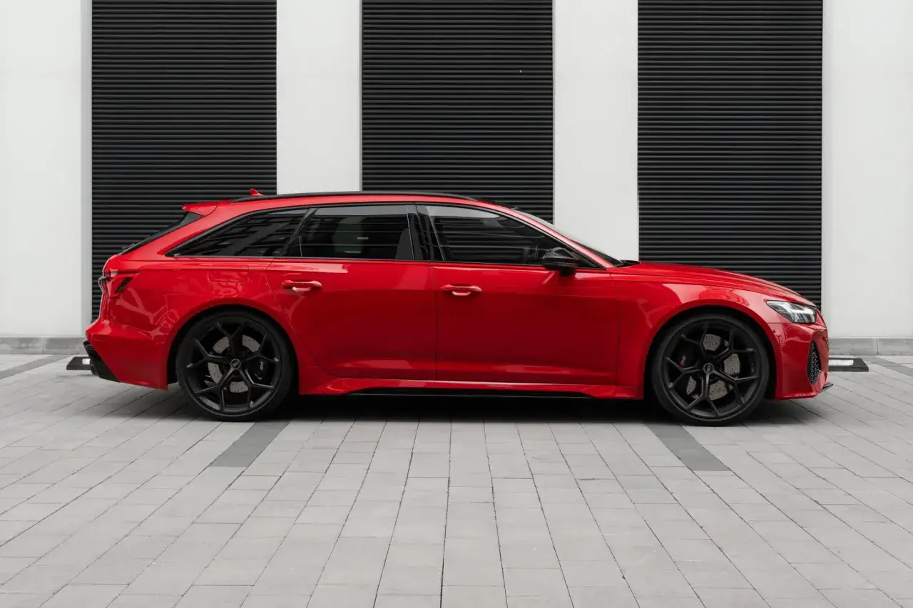 Czerwone Audi RS6 Avant z czarnymi felgami stoi na tle nowoczesnej, geometrycznej ściany.