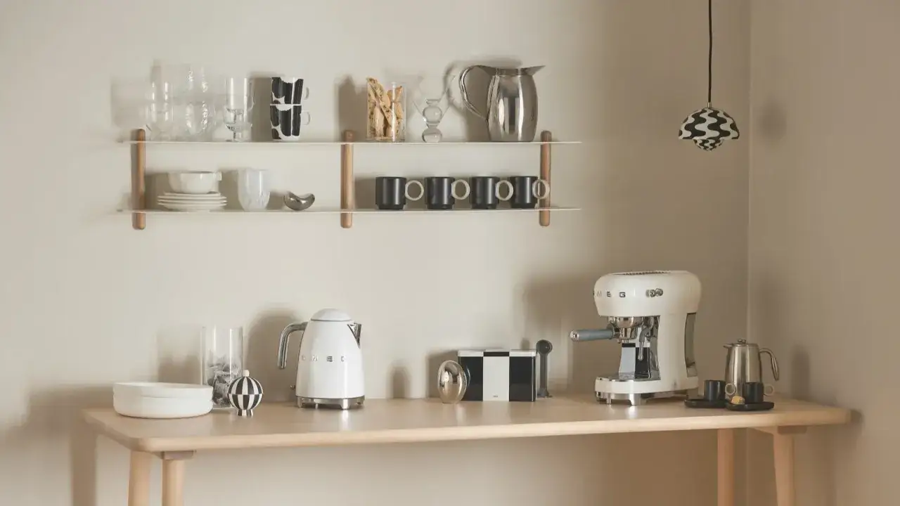 En stilren kaffebar hemma med vit espressomaskin, vattenkokare och snygga muggar på hyllor.