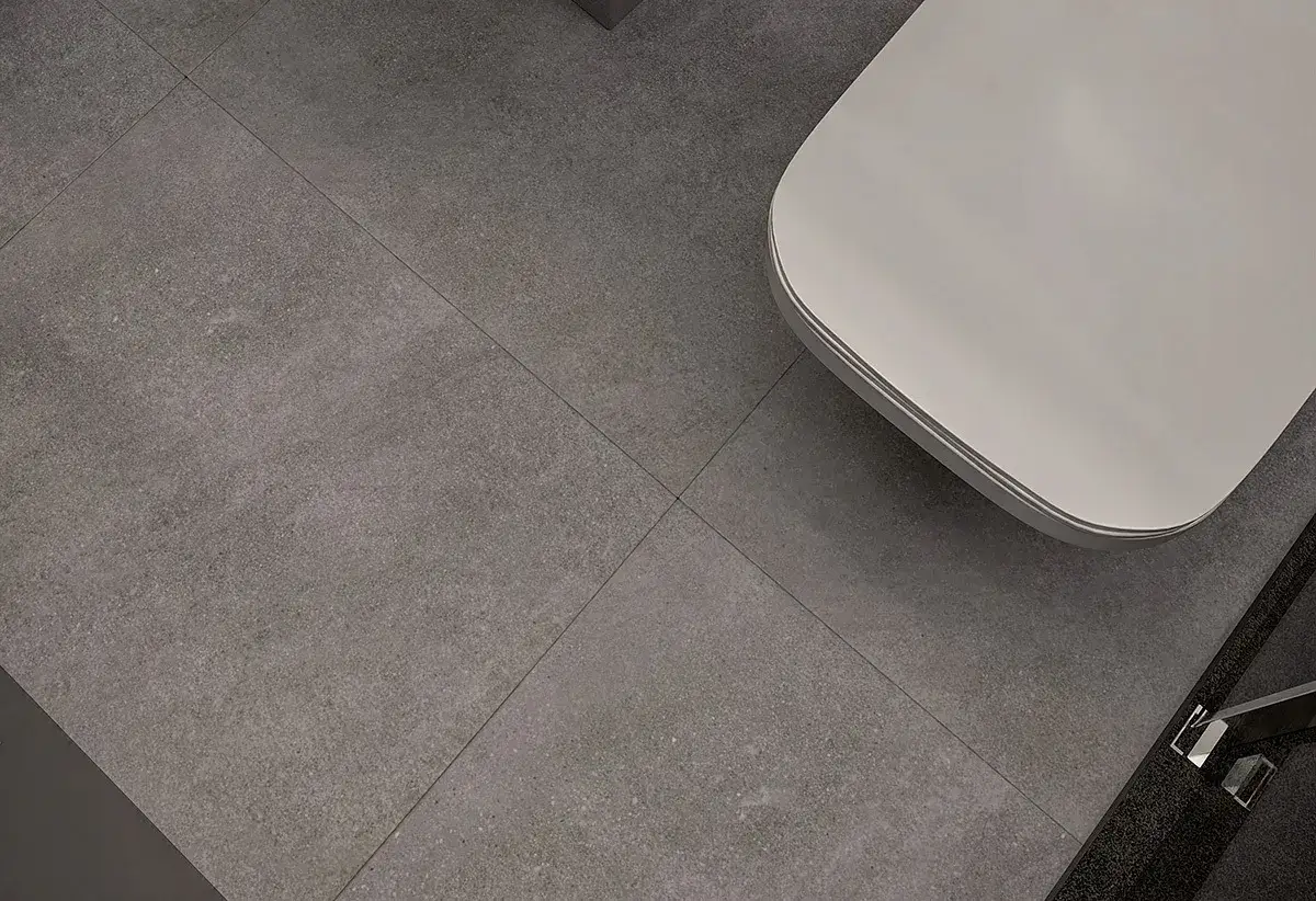 Szara podłoga z gresu 60x60, z widocznym fragmentem białej wanny. Fuga jest wąska, podkreślając nowoczesny charakter wnętrza.