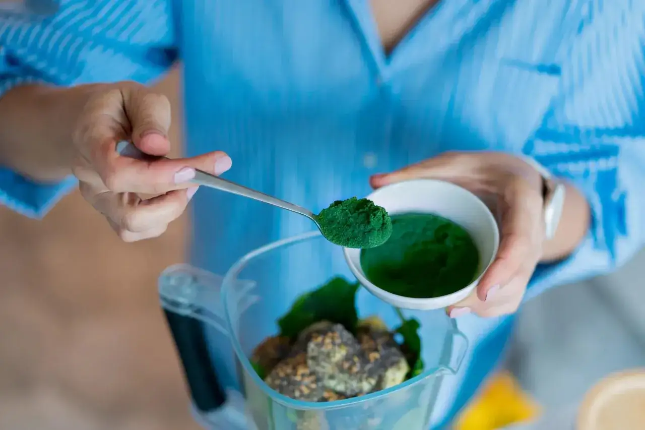 Dodawanie zielonego proszku do blendera. To spirulina, superfood, który wzbogaci Twój koktajl.