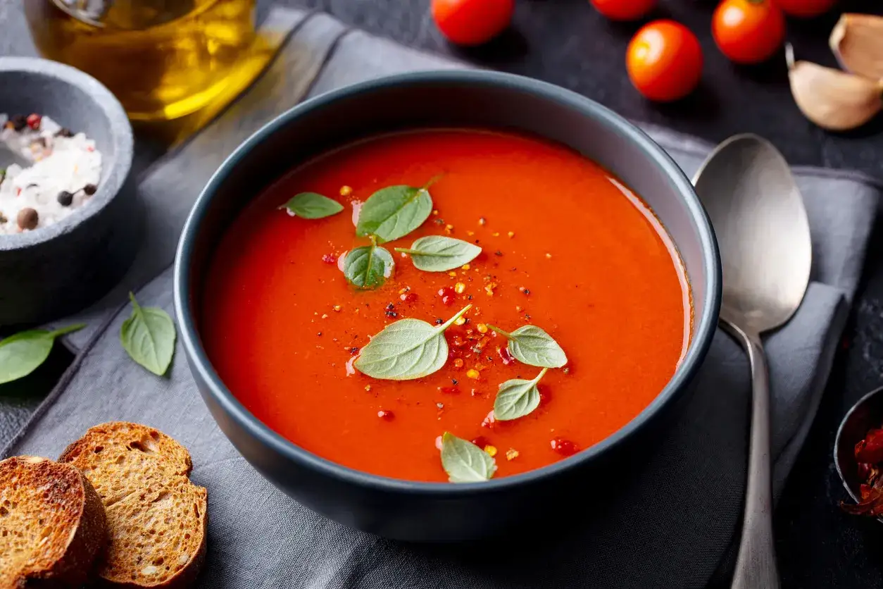 Aksamitna węgierska zupa paprykowa, udekorowana listkami bazylii i płatkami chili, podana z grzankami.
