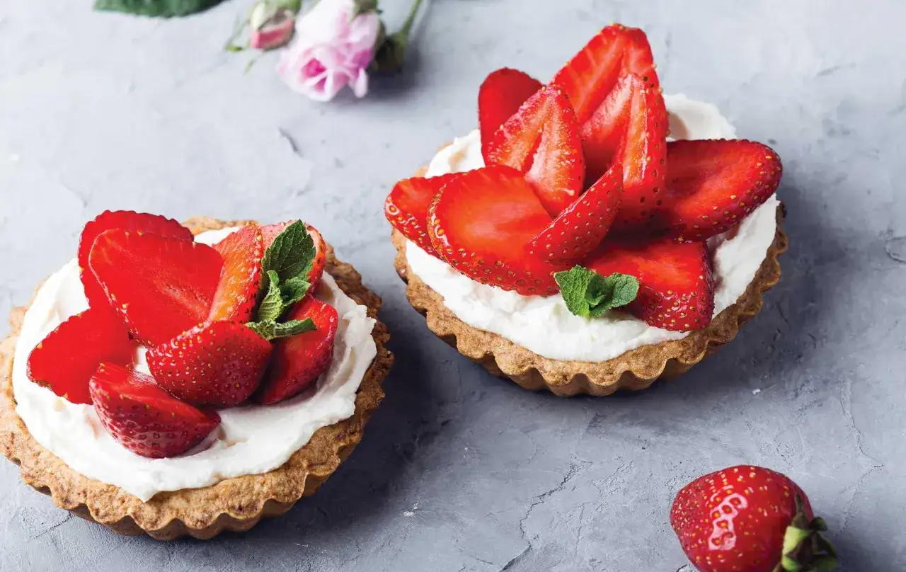 Deux tartelettes garnies de chantilly mascarpone et de fraises fraîches, décorées de feuilles de menthe.