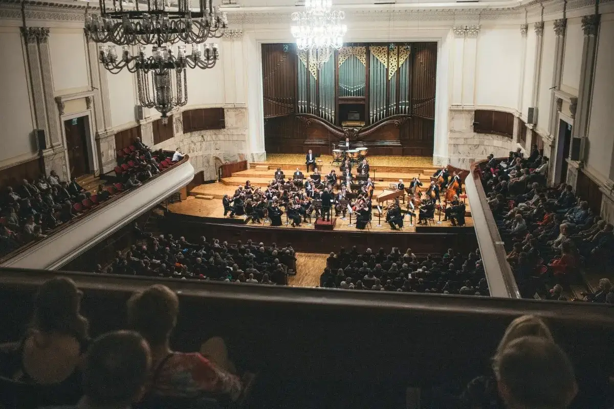 Koncert w filharmonii. Orkiestra gra na scenie, a publiczność słucha w wypełnionej sali.