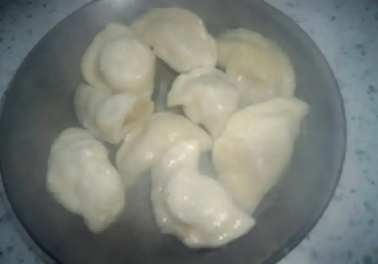 Parująca miska z ugotowanymi pierogami. Ciasto na pierogi jest miękkie i apetyczne, gotowe do podania.