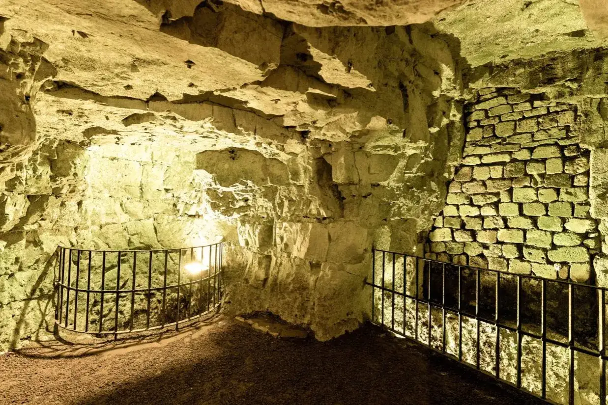 Des passages souterrains éclairés, vestiges des boves d'Arras, avec des murs en pierre brute et des murets en briques.