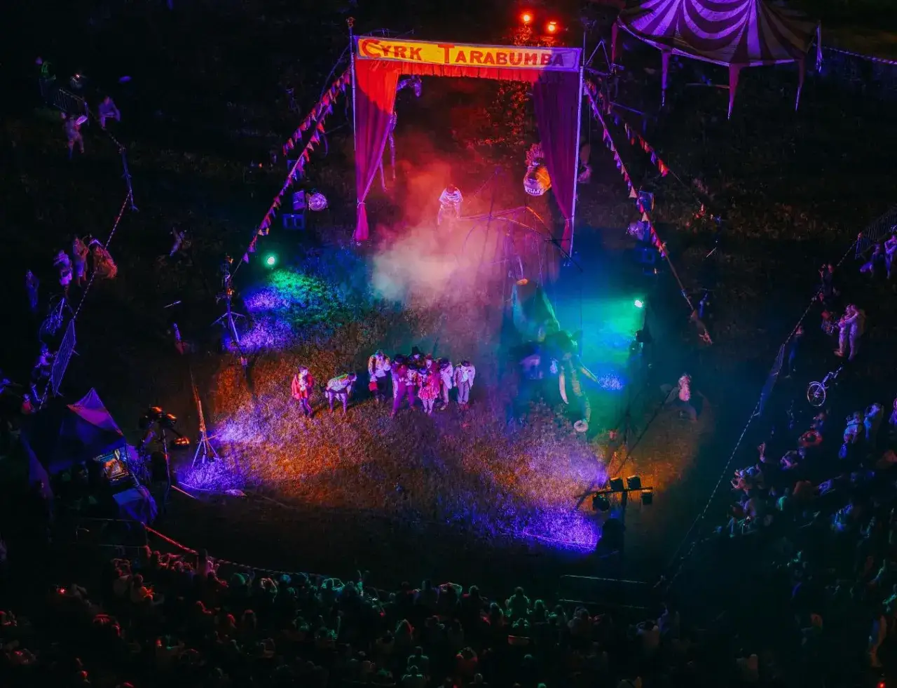 Kolorowy, nocny pokaz cyrkowy na festiwalu. Widać artyst&oacute;w, słonie i publiczność.