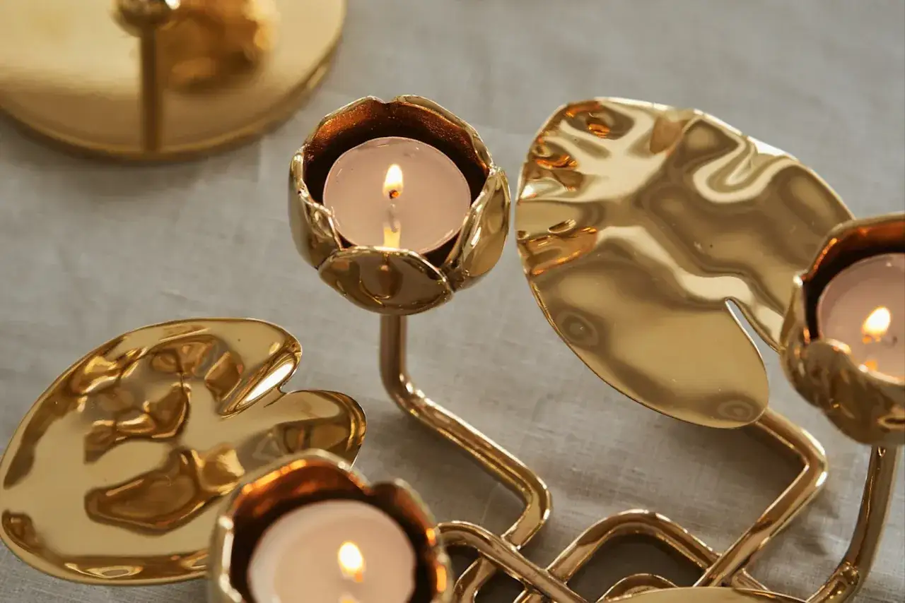 Gyllene ljusstakar i Hilke collection, formade som n&auml;ckrosblad och knoppar, med t&auml;nda v&auml;rmeljus.