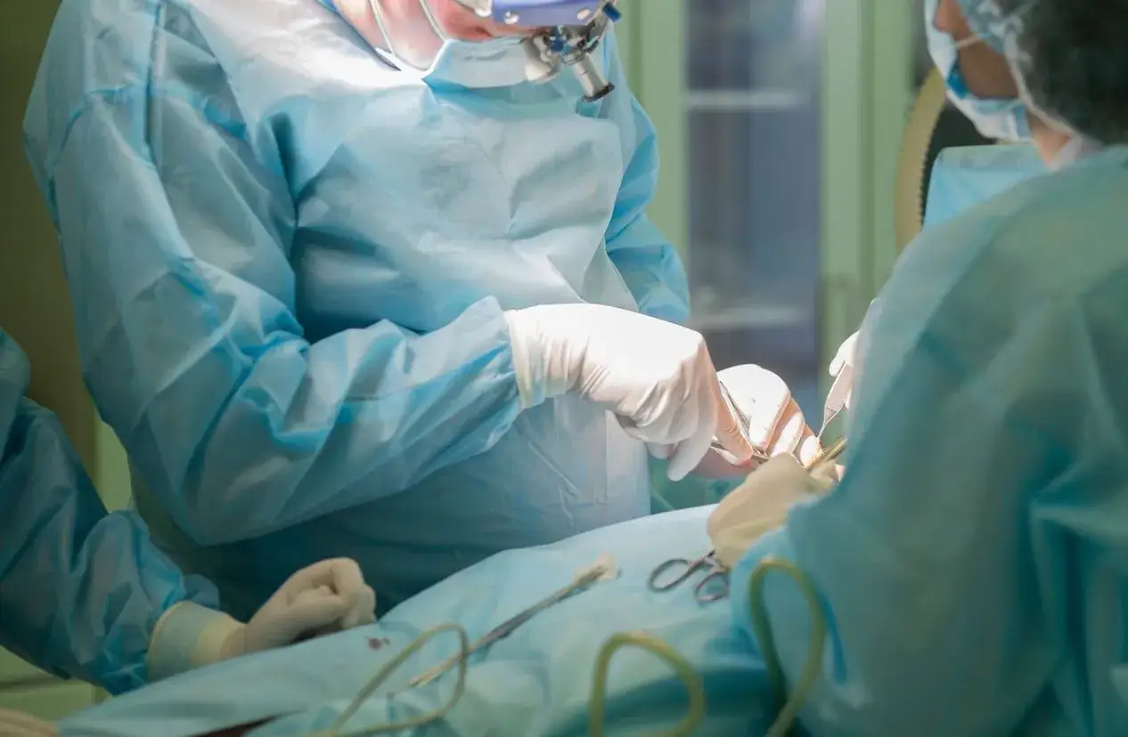 Chirurdzy w sterylnych ubraniach pracują przy pacjencie. W tle widać sprzęt medyczny, sugerujący operację, być może związaną z powikłaniami po aquafilling.