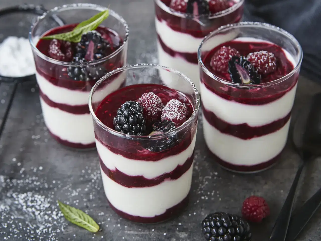 Schichtdessert mit Beeren und cremiger Creme Double, bestäubt mit Puderzucker.