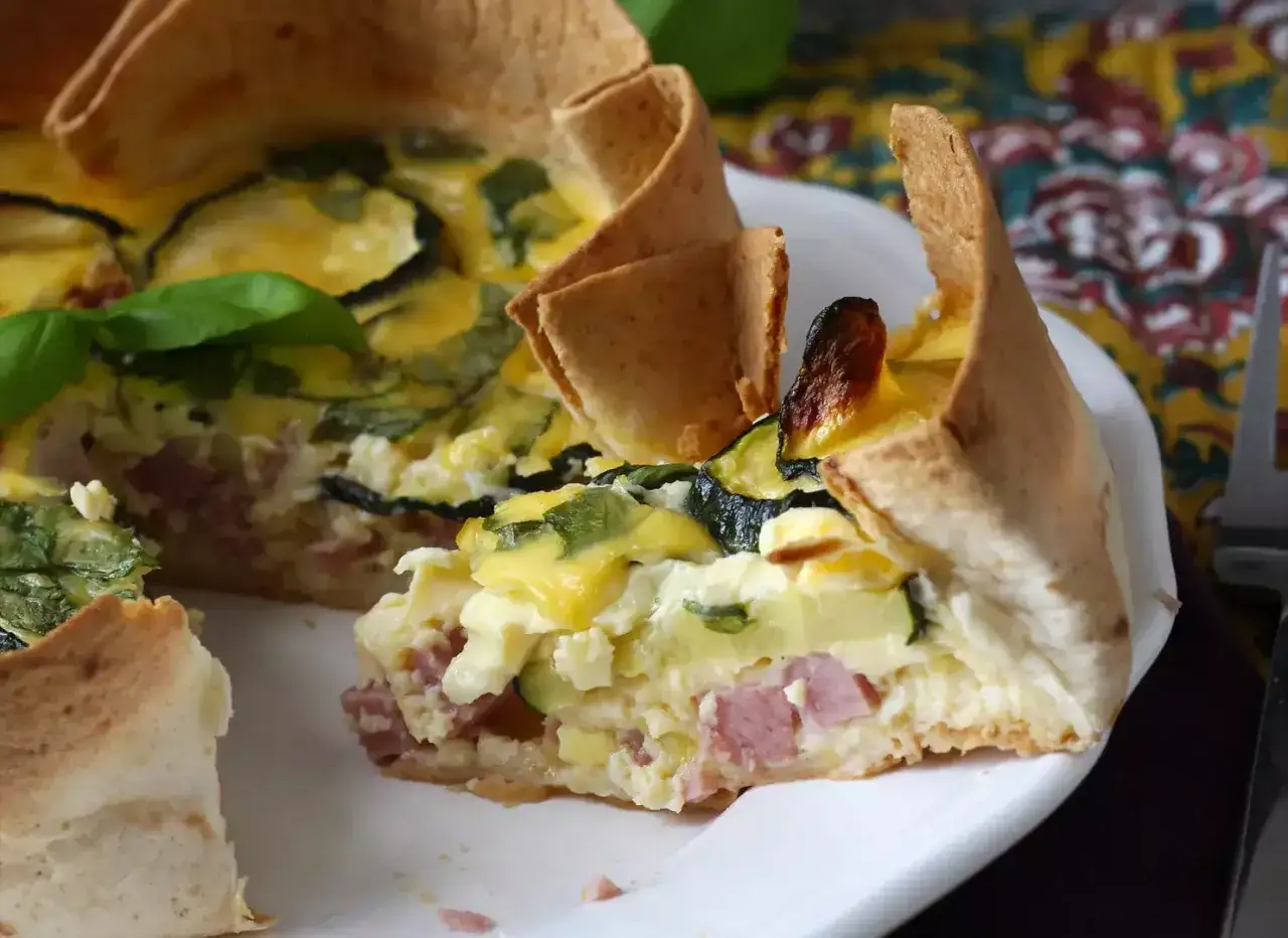 Une part de quiche wrap aux courgettes et jambon, garnie de basilic frais, sur une assiette blanche.