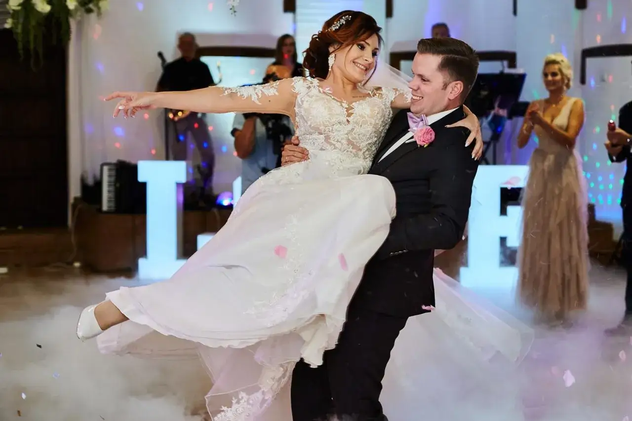 Młoda para tańczy pierwszy taniec. Pan młody niesie pannę młodą, a w tle świecą litery LOVE. Idealny moment na rockowe piosenki na pierwszy taniec.