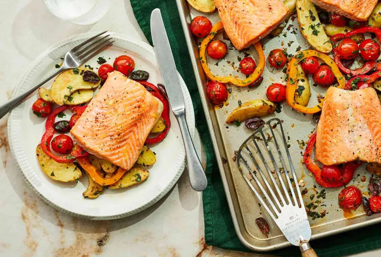 Salm&oacute;n al horno con verduras: patatas, pimientos y tomates cherry asados, servidos en un plato y en una bandeja.