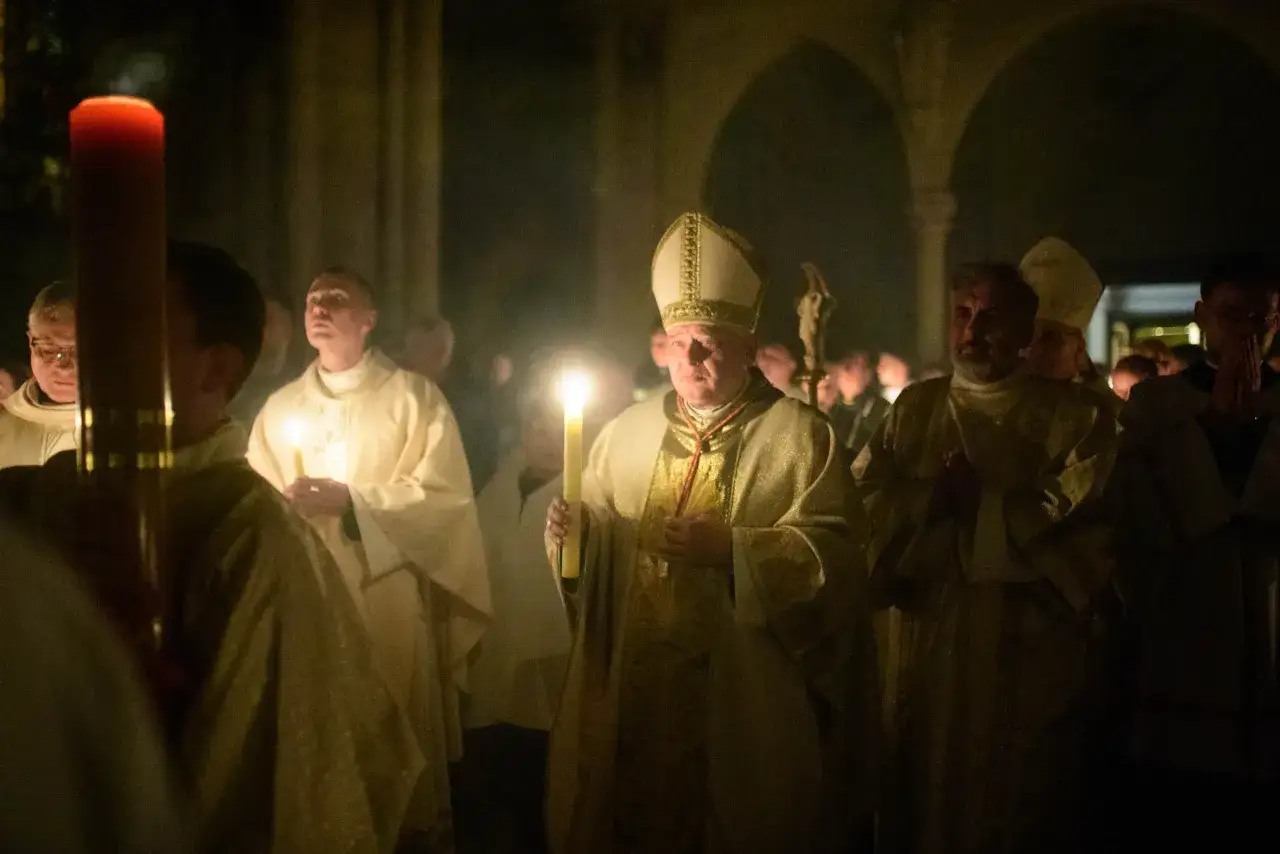 Biskup z mitrą i wierni z zapalonymi świecami podczas nabożeństwa. Czy msza w Wielką Sobotę jest obowiązkowa?