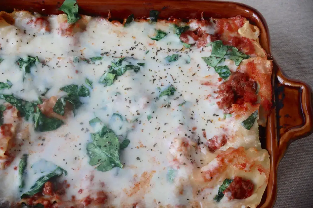 En krämig salsiccia lasagne med gröna blad och smält ost, redo att avnjutas.
