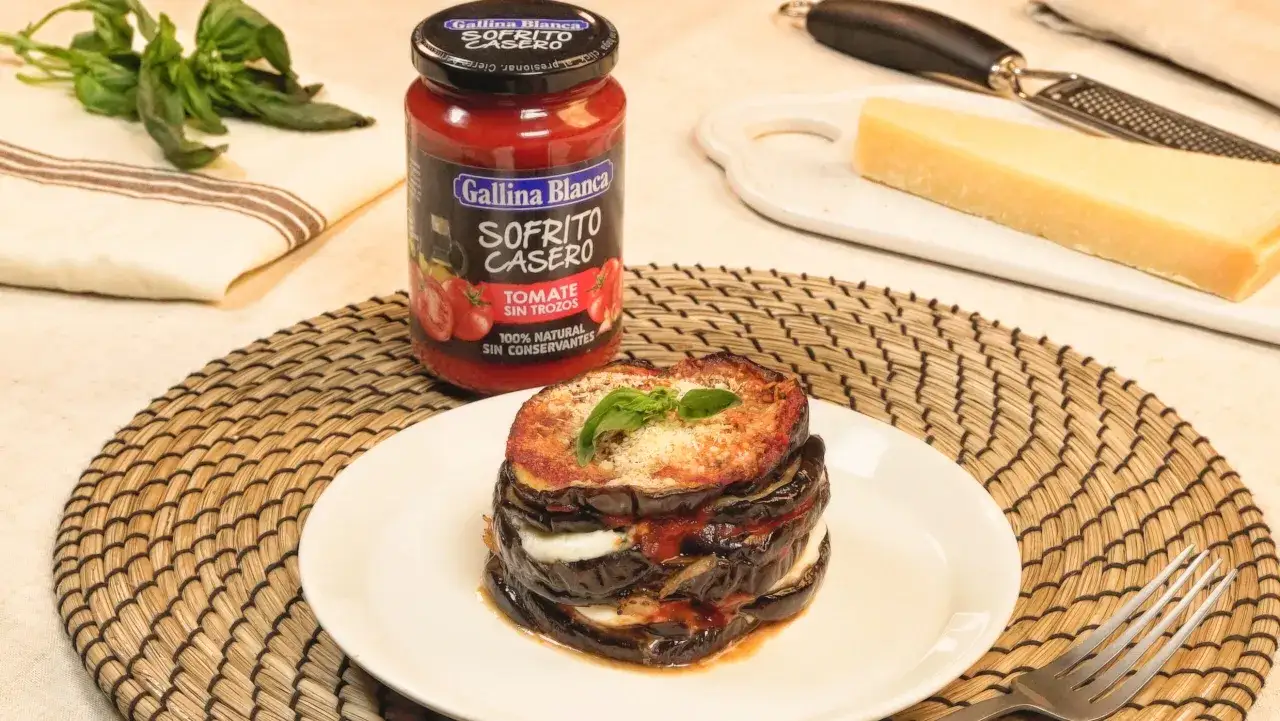 Parmigiana di melanzane apilada, con sofrito casero, queso y albahaca. Ingredientes frescos para un plato delicioso.