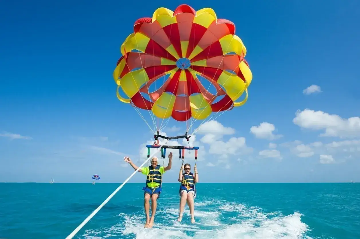 Parasailing na Teneryfie to świetne atrakcje dla dzieci i dorosłych. Dwie osoby szybują nad turkusowym morzem pod kolorowym spadochronem.