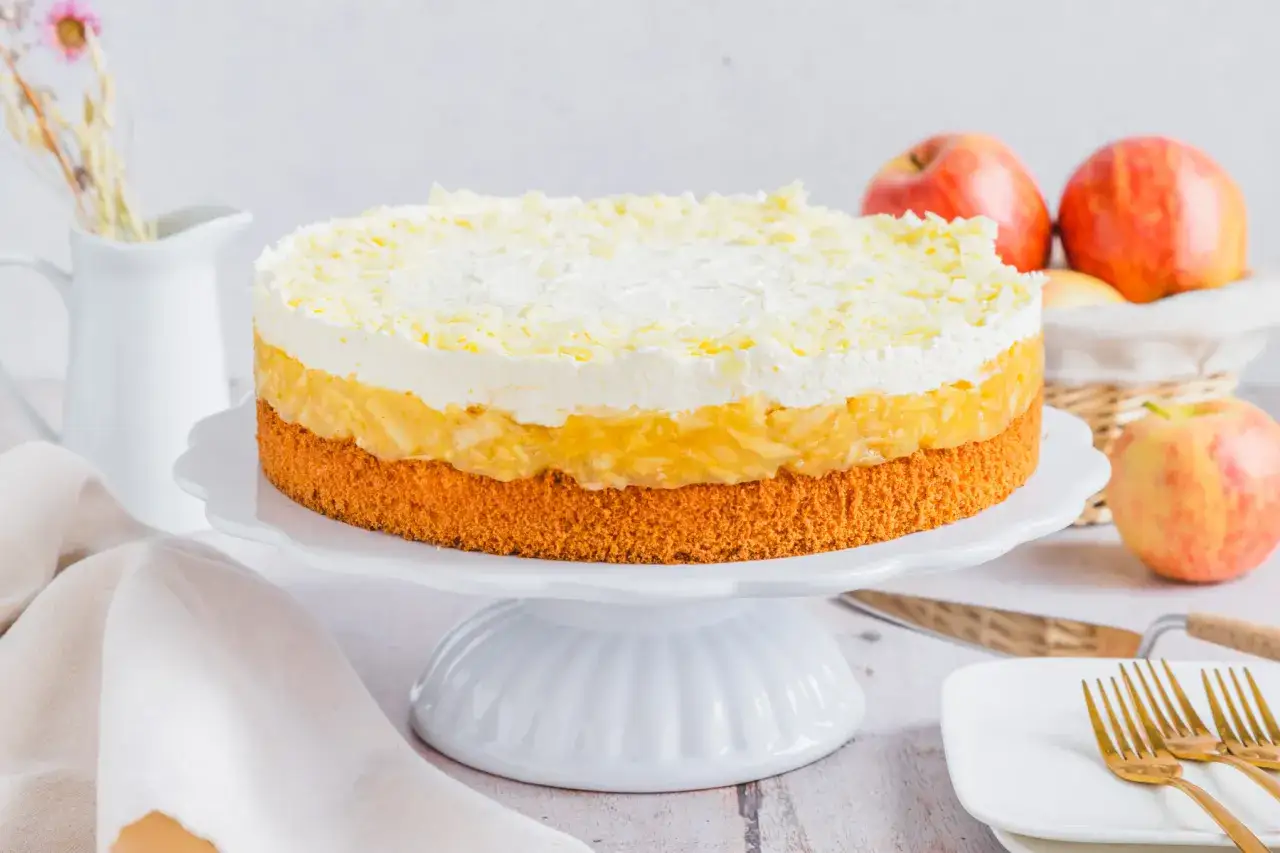 Schwedische Apfeltorte mit drei Schichten: Biskuitboden, Apfelmus und Sahnehaube, bestreut mit wei&szlig;en Schokostreuseln.