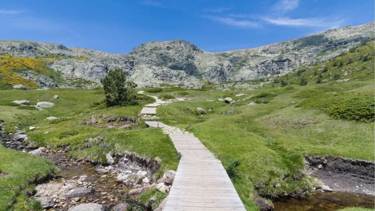 Sendero de madera serpentea por un paisaje montañoso verde, ideal para rutas senderismo Madrid.