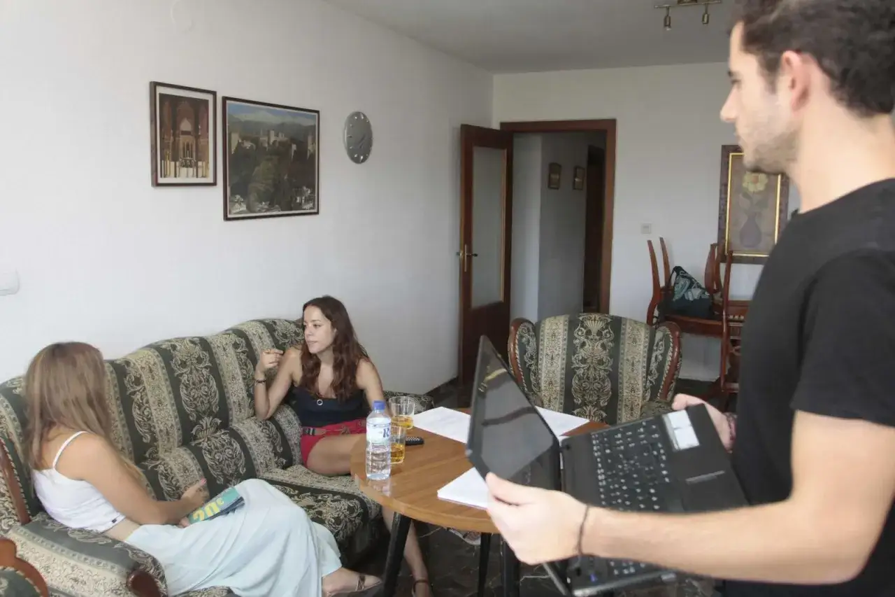Un hombre con un port&aacute;til se acerca a dos mujeres sentadas en un sof&aacute;, discutiendo el articulo 4 lau.