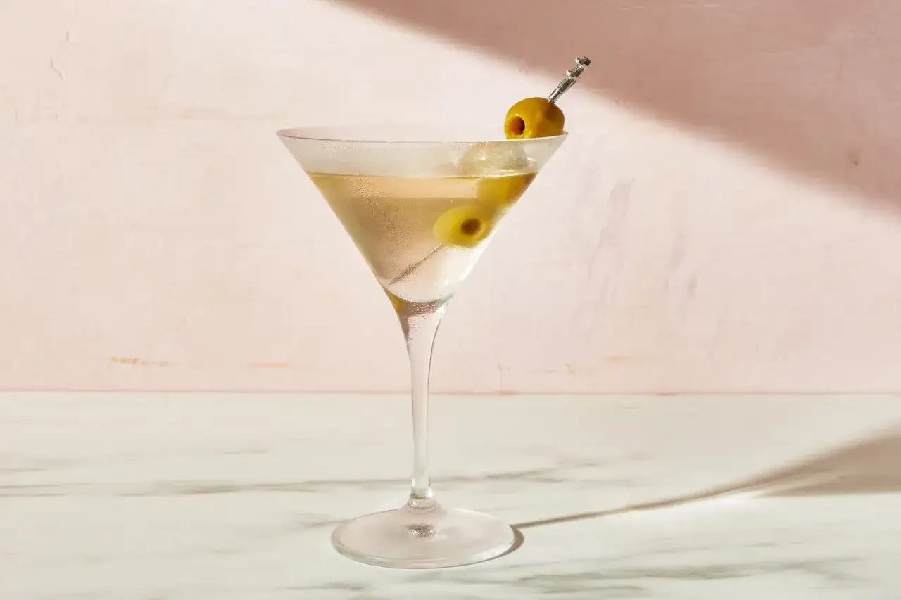 Un verre à martini rempli d'un cocktail clair, garni de deux olives sur une pique. Une invitation à découvrir la recette du dirty martini.