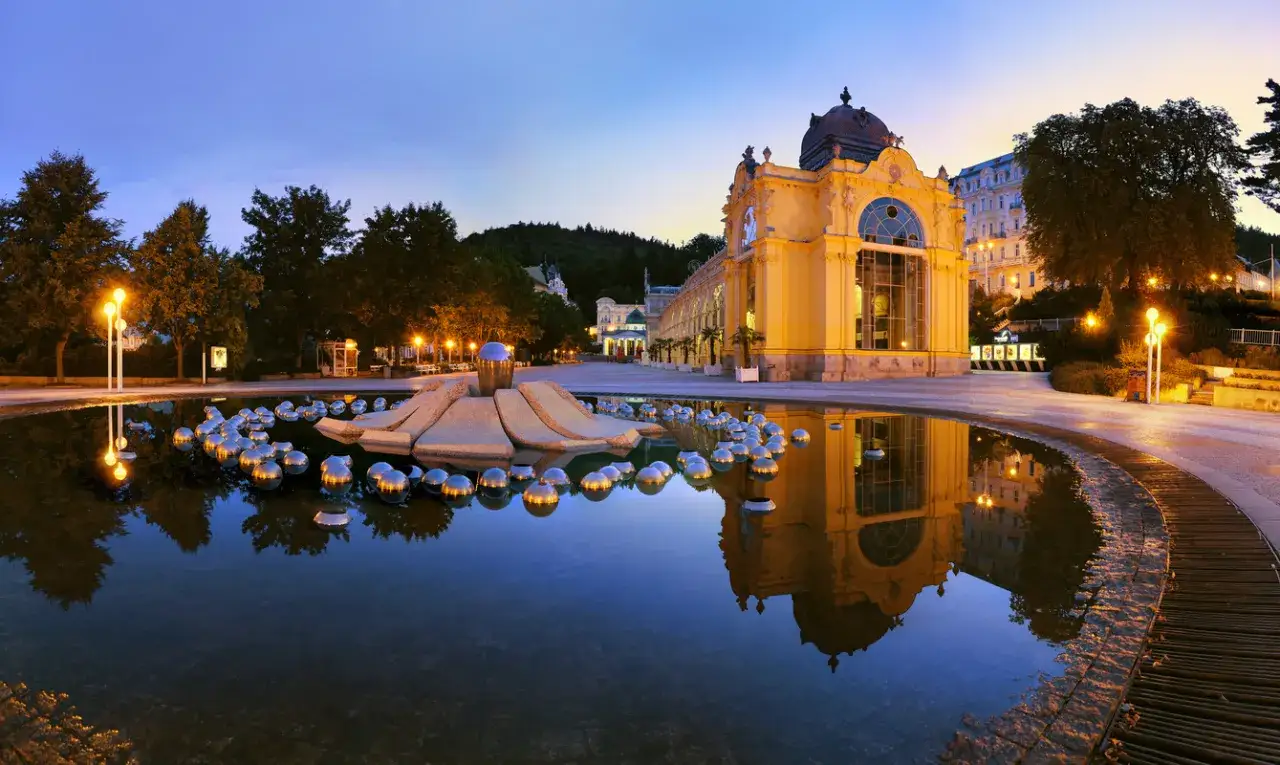 Abendliche Ansicht einer Therme in Tschechien mit einem Brunnen voller Kugeln und einem gelben Gebäude im Hintergrund.