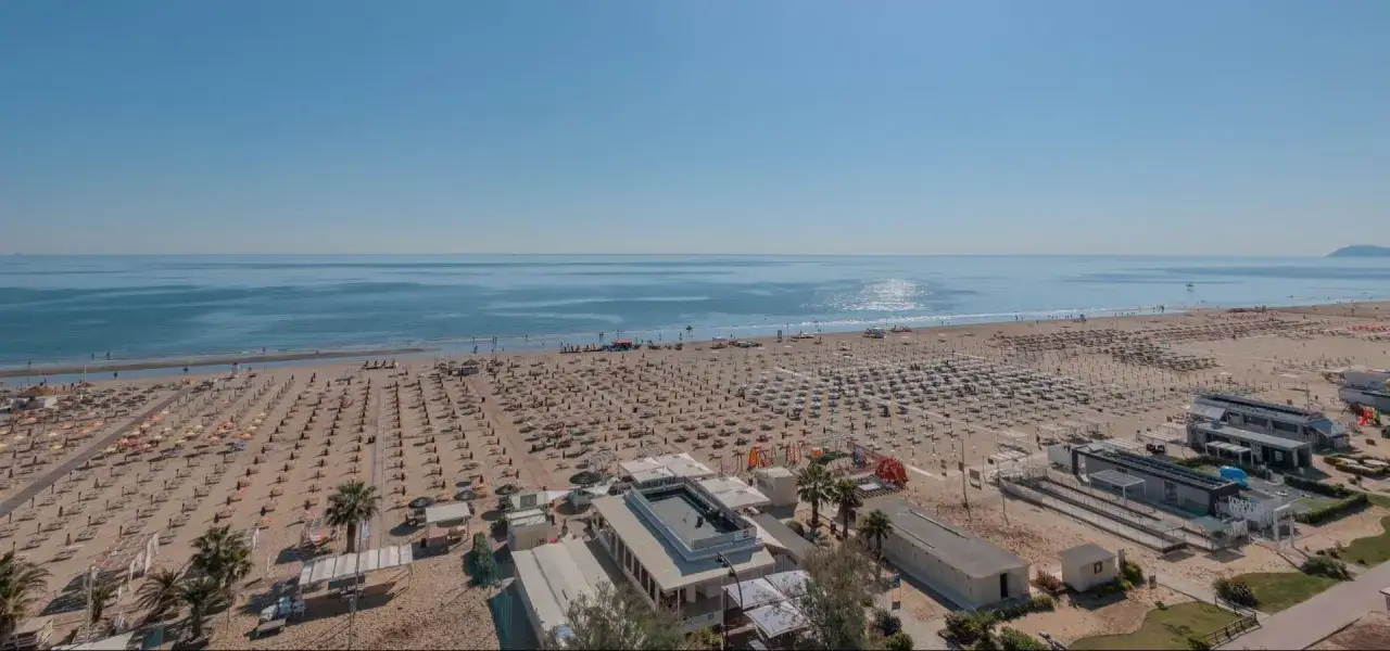 Ampia spiaggia attrezzata a Rimini Miramare, con file ordinate di ombrelloni e lettini che si estendono fino al mare calmo e azzurro.
